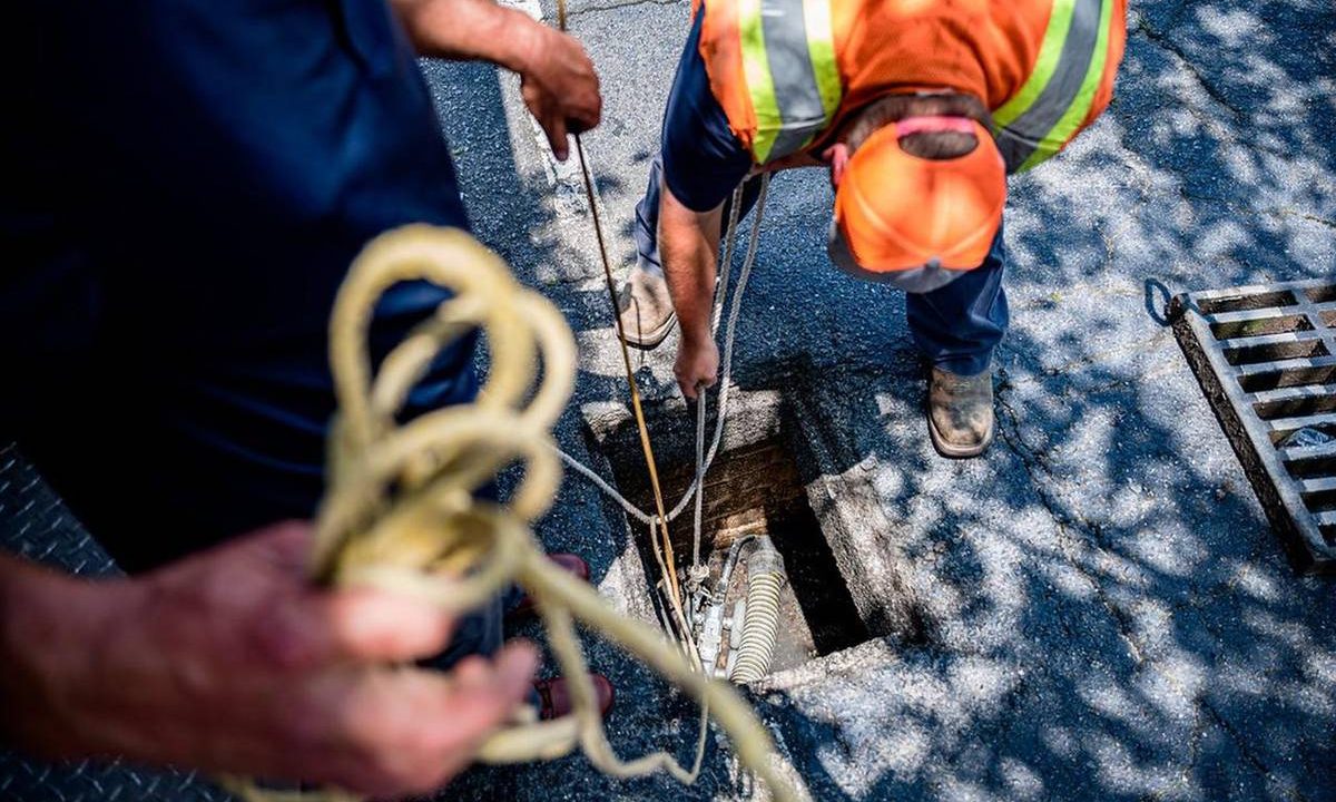 Fachkraft führt Prüftechnik in einen geöffneten Schacht ein