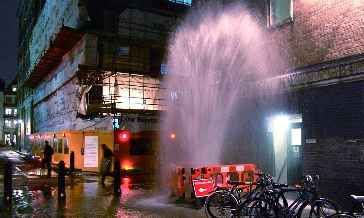 Wasserfontäne aus einer gebrochenen Leitung auf einer Straße bei Nacht