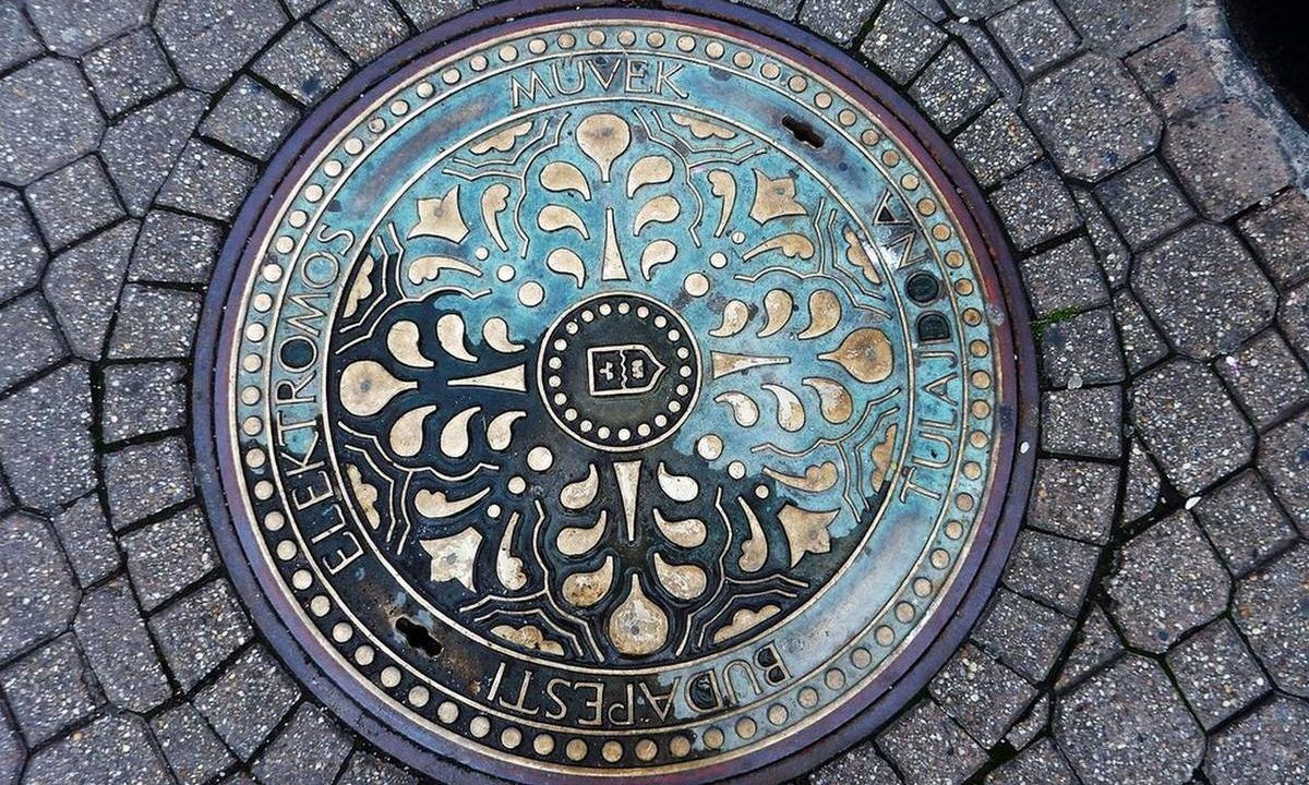 Verzierter Kanaldeckel im Kopfsteinpflaster